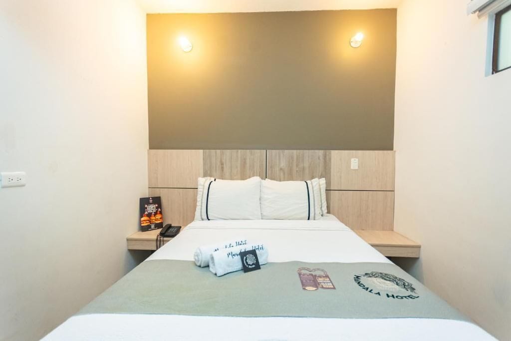 A hotel room with a bed, a bedside table, a wall-mounted light, and a framed picture.