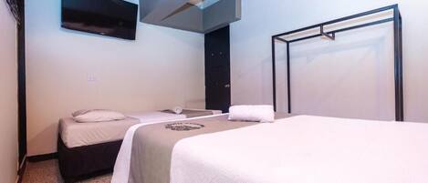 A hotel room with two beds, a TV mounted on the wall, and a door.