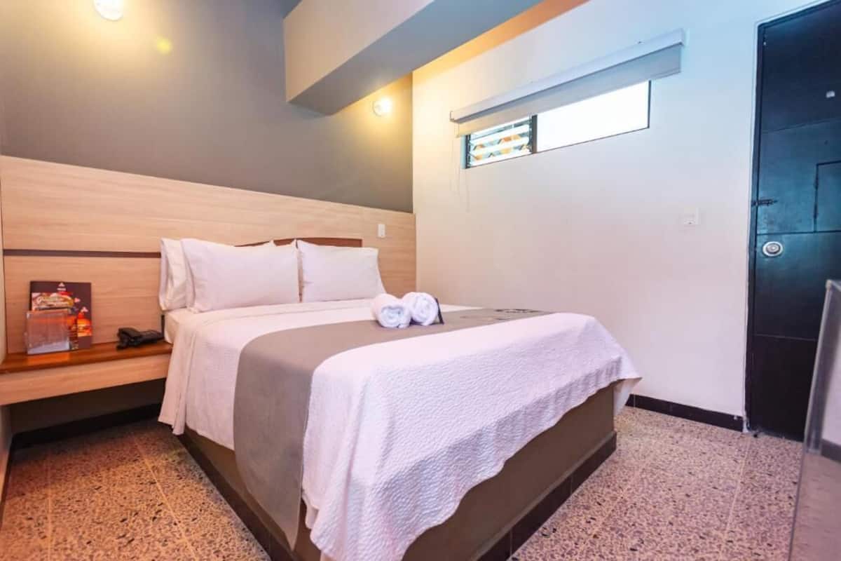 A hotel room with a bed, bedside table, and a small window.