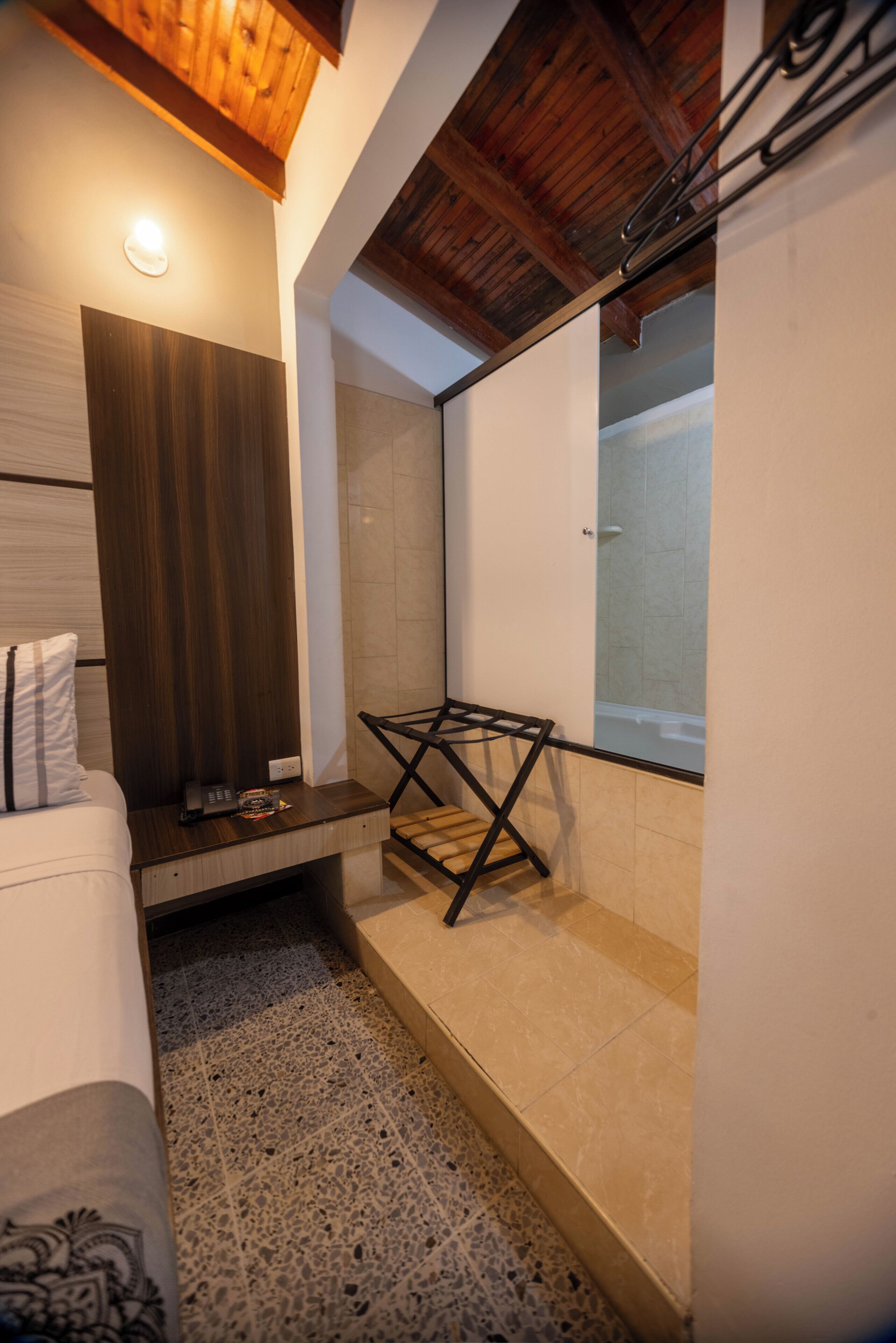 A modern bathroom with a wooden ceiling, a shower with a glass door, and a small seating area with a towel rack.