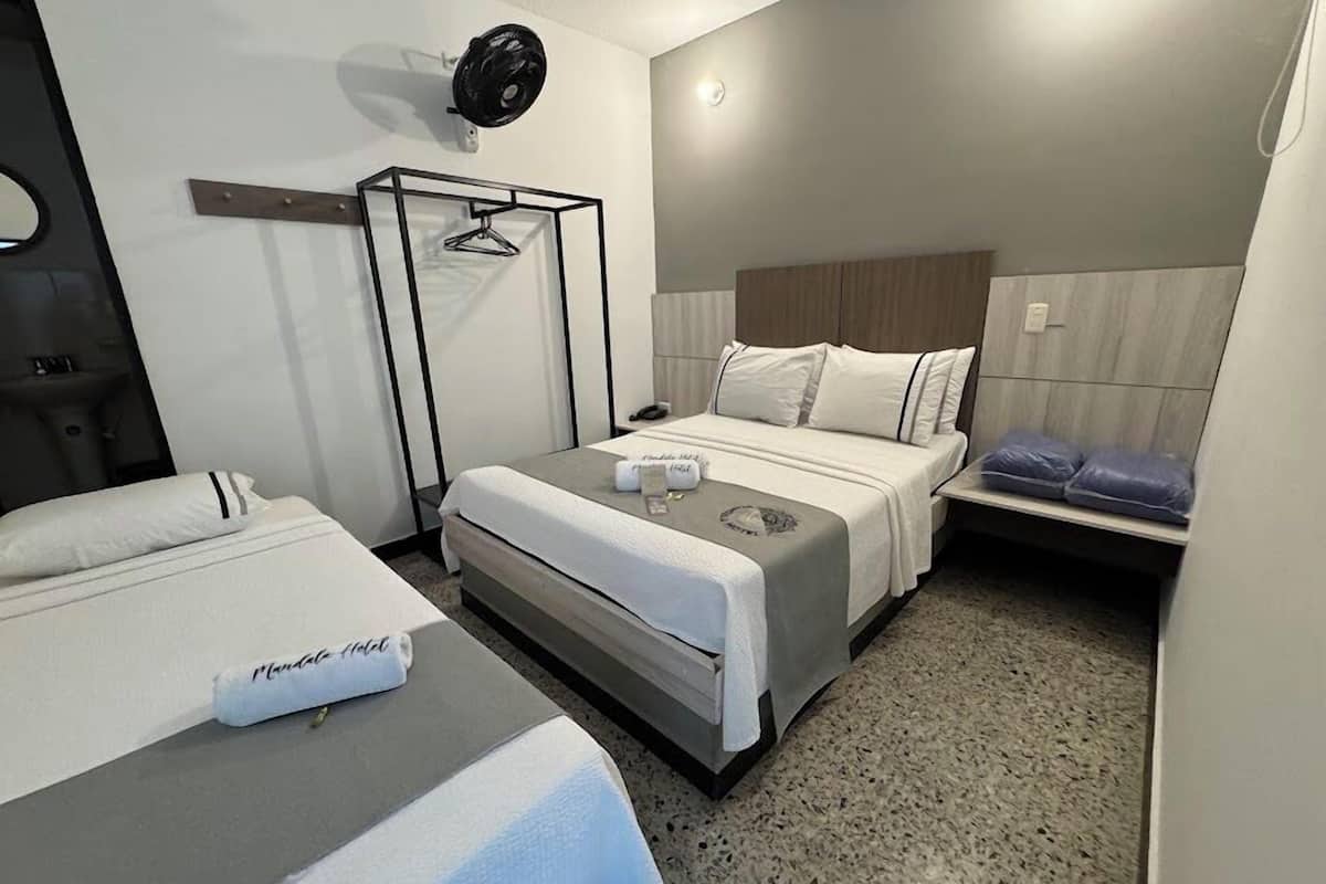 A hotel room with a bed, a bedside table, a hanging light fixture, and a small seating area with cushions.