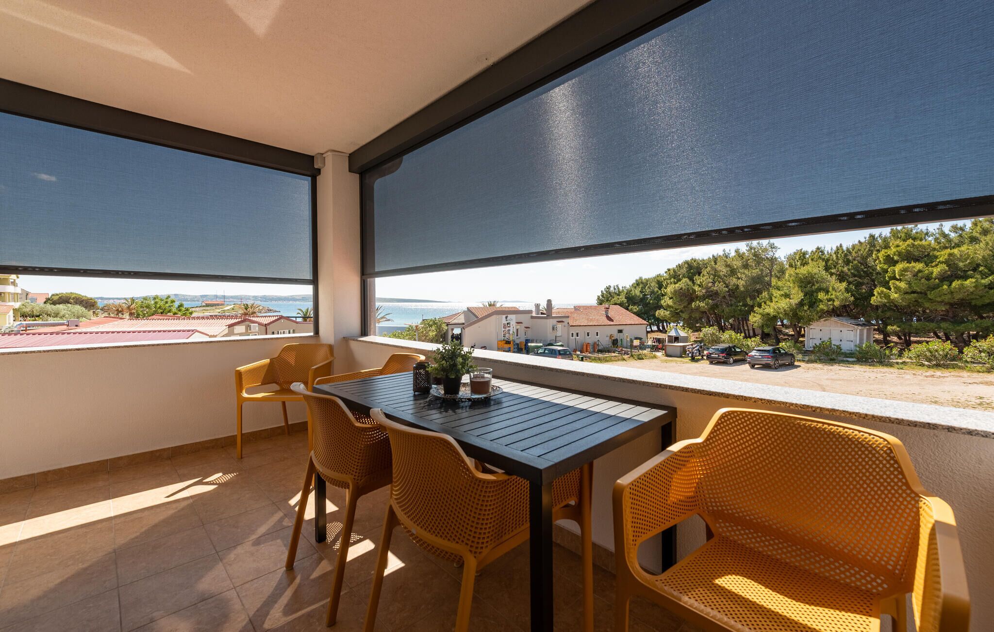 Un balcón con mesa y sillas, con vistas a una zona costera con edificios y árboles.
