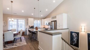 A modern kitchen with white cabinets, stainless steel appliances, and pendant lighting.