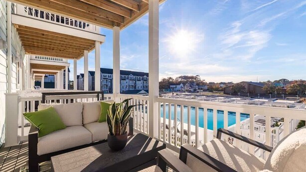 A covered outdoor seating area with a pool view, white railings, and a clear sky.