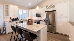 A modern kitchen with white cabinetry, a central island with bar stools, stainless steel appliances, and pendant lighting.