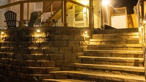 Un ensemble de marches en pierre, agrémentées d’un éclairage extérieur, menant à un espace abrité où se trouvent des fauteuils Adirondack.