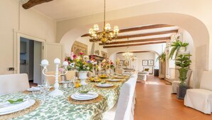 Een eetruimte met een lange tafel gedekt voor een maaltijd, met een kroonluchter, bloemrijke decoraties en een rustiek plafond.