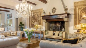 Een knusse woonkamer met een open haard, comfortabele banken, een kroonluchter en decoratieve wandkunst.