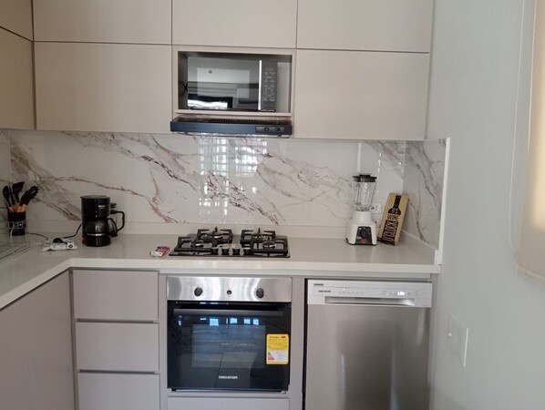 Een moderne keuken met een gasfornuis, koffiezetapparaat, blender en vaatwasser.