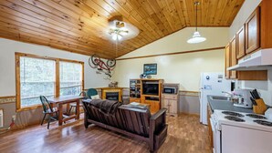 A compact kitchen with wooden cabinets, a dining area with a sofa, and a TV.