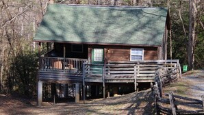 A rustic cabin with a green roof, a wooden deck, and a single window.