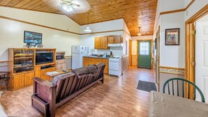A cozy interior with a wooden ceiling, a sofa, a dining table, and a kitchen area with cabinets and appliances.
