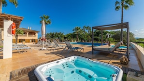 Zona de piscina con sillones reclinables, un jacuzzi y una zona de estar techada.