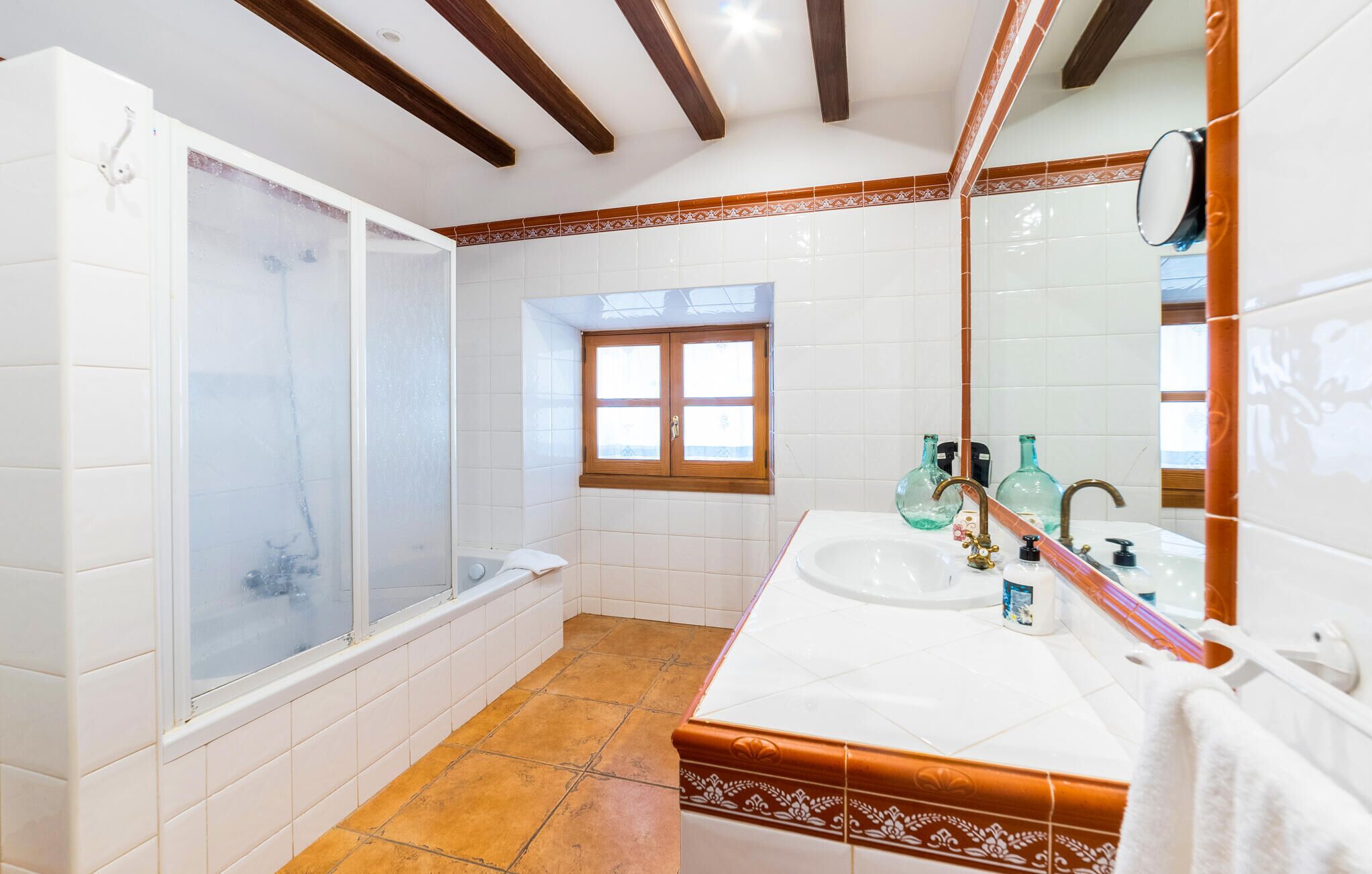 Une salle de bain avec une douche, une fenêtre et un lavabo avec deux bouteilles.