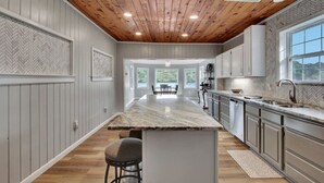 A kitchen with a wooden ceiling, white cabinets, a marble island, and a view to the outside. - Lake Haven (Hot Tub, Game Room) (Hot Springs)
