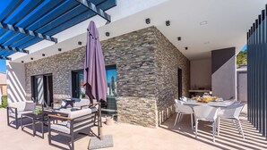 Une terrasse extérieure moderne, avec des murs en pierre, un espace salon couvert et un coin repas aménagé.