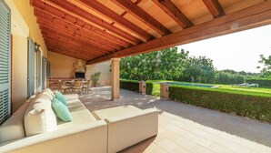 Un patio couvert avec un canapé, du mobilier d’extérieur et une vue sur une piscine et un jardin.