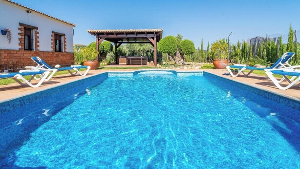 A swimming pool with lounge chairs, a pergola, and a house in the background. - Villa Hermanas Algodonales by Ruralidays (Cádiz)