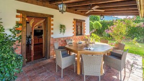 A covered patio with a round wooden table and wicker chairs, a brick wall, and potted plants. - Villa Hermanas Algodonales by Ruralidays (Cádiz)