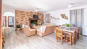 A spacious living room with a fireplace, a dining area with wooden furniture, and a kitchen area. - Los tres picos Prado del Rey by Ruralidays (Cádiz)