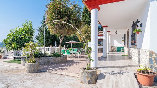 A covered outdoor area with stone planters, green chairs, and a white building with red accents. - Los tres picos Prado del Rey by Ruralidays (Cádiz)