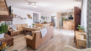 A spacious living room with a sofa set, a dining table, and a kitchen area with a brick accent wall. - Los tres picos Prado del Rey by Ruralidays (Cádiz)