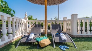 Two sun loungers with towels and a hat, a small table, and a thatched umbrella in a well-maintained outdoor area with white balustrades and greenery. - Los tres picos Prado del Rey by Ruralidays (Cádiz)