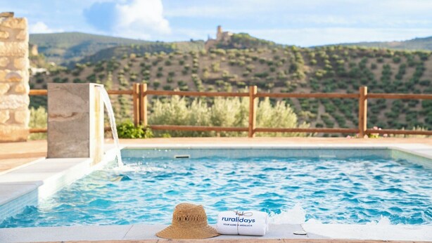 Una piscina con recinzione in legno e muro in pietra, un cappello e un asciugamano sul bordo.