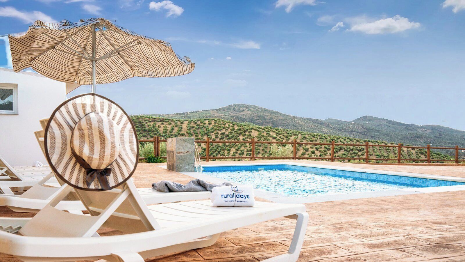 A poolside area with a lounge chair, an umbrella, and a sign for 'Ruraltur Holidays'.