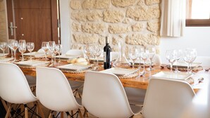 Un tavolo da pranzo apparecchiato con bicchieri da vino, piatti e una bottiglia, circondato da sedie bianche in una stanza con una parete in pietra e una porta in legno.