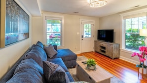 Ein Wohnzimmer mit einem grauen Sofa, einem Fernseher und einem Holzschrank.
