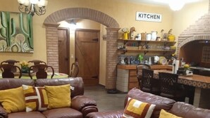 A living room with two brown leather sofas, a chandelier, a kitchen area with a brick oven, and a dining area with a table and chairs. - Huerta Ariana  (Parras de la Fuente)