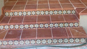 A welcome sign above a wooden door, flanked by two wicker chairs with cushions, leading to a tiled entrance. - Huerta Ariana  (Parras de la Fuente)