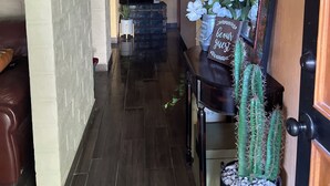 A hallway with a wooden floor, a black bench, a cactus plant, and a sign that reads "be our guest". - Huerta Ariana  (Parras de la Fuente)