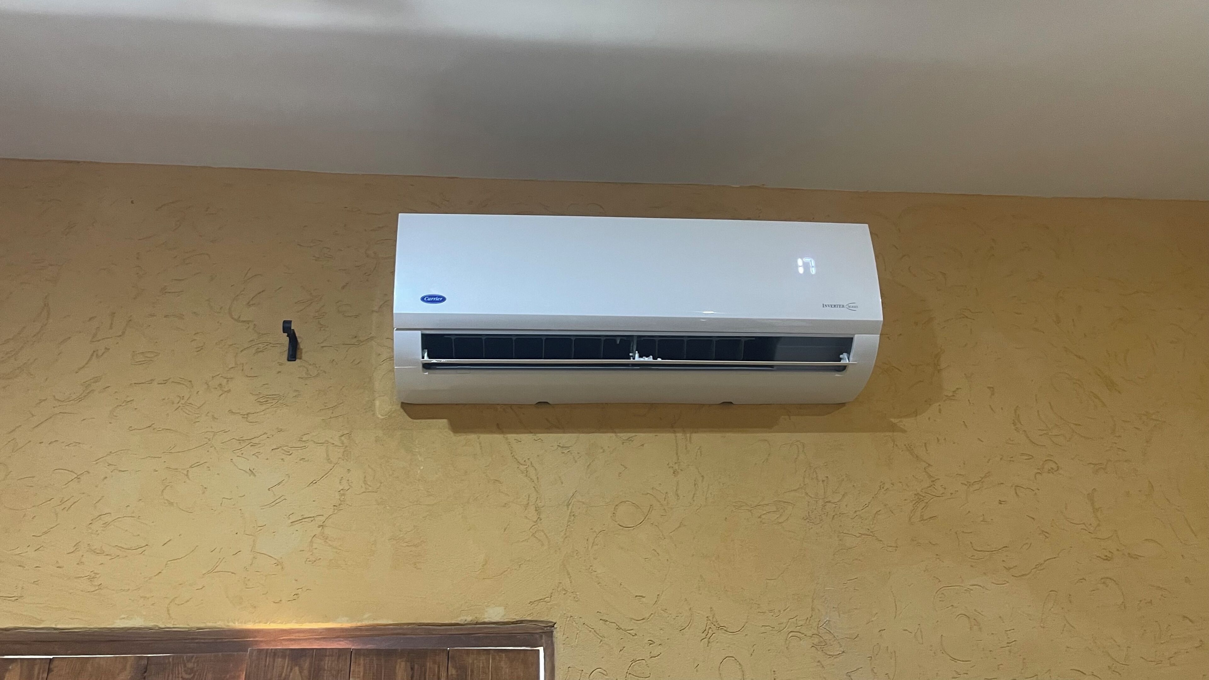 Un climatiseur blanc fixé sur un mur beige à texture.