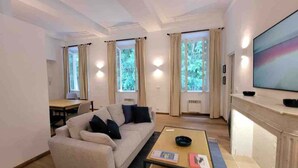 A modern living room with a sofa, a coffee table, and a TV. There are windows with curtains and a fireplace.