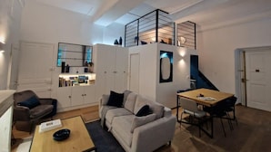 A compact living space with a sofa, a dining table, a kitchen area, and a staircase leading to an upper level.