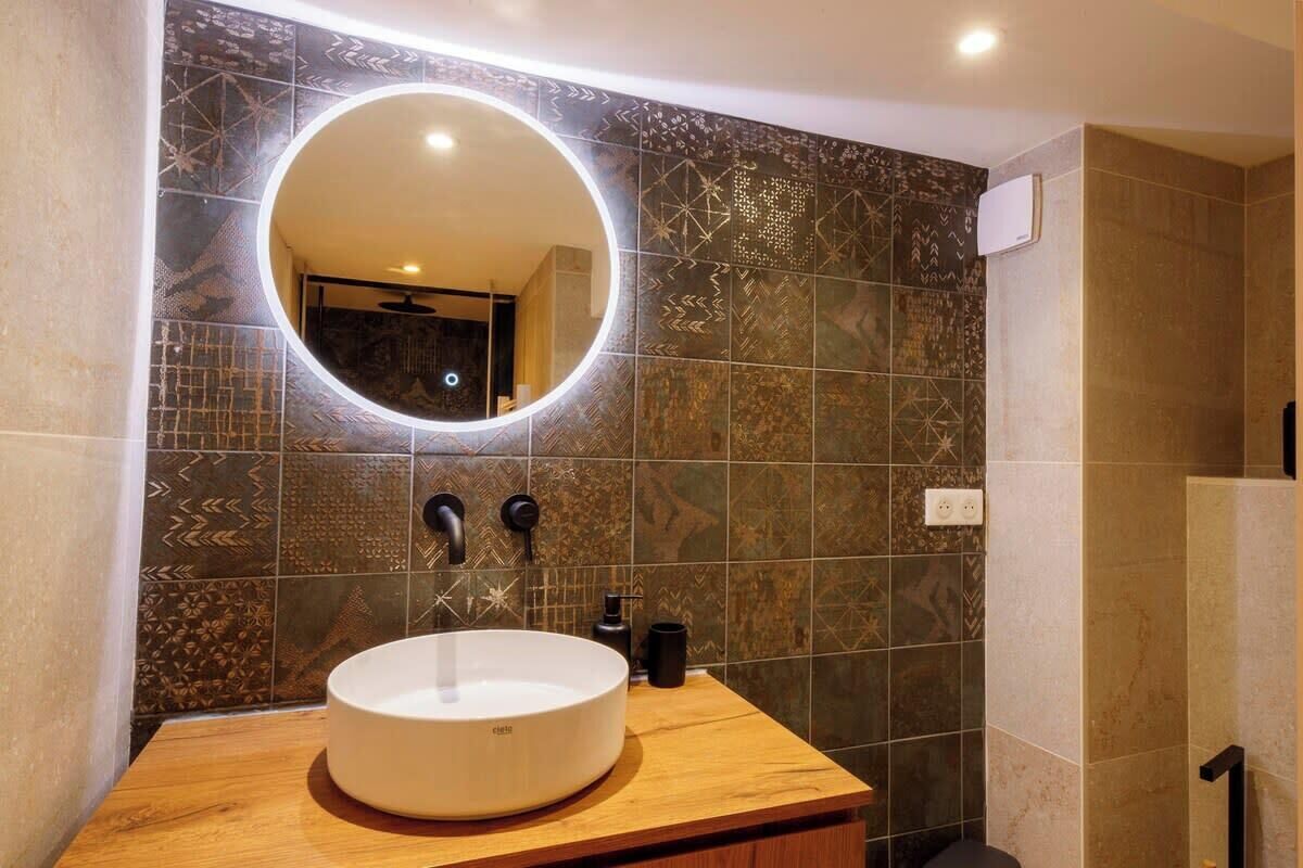 Un baño con un espejo redondo, un lavabo blanco y azulejos estampados.
