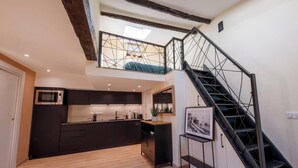 Eine moderne Küche mit dunklen Schränken, Holzboden und einer schwarzen Treppe, die in ein Obergeschoss führt.