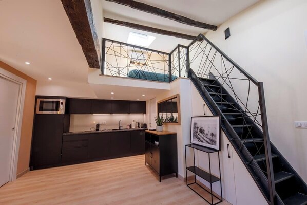 A modern kitchen with dark cabinets, a wooden floor, and a black staircase leading to an upper level.