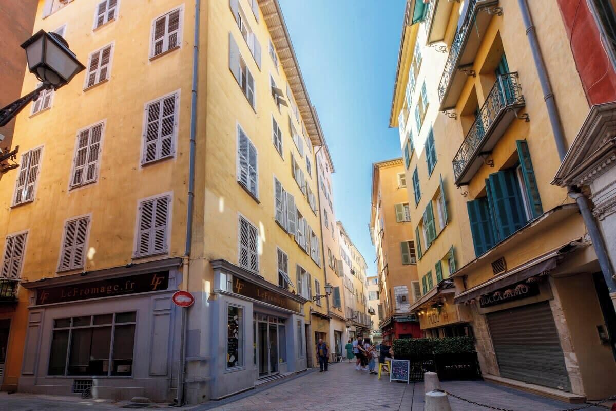 A narrow street with yellow buildings, storefronts, and a clear sky.