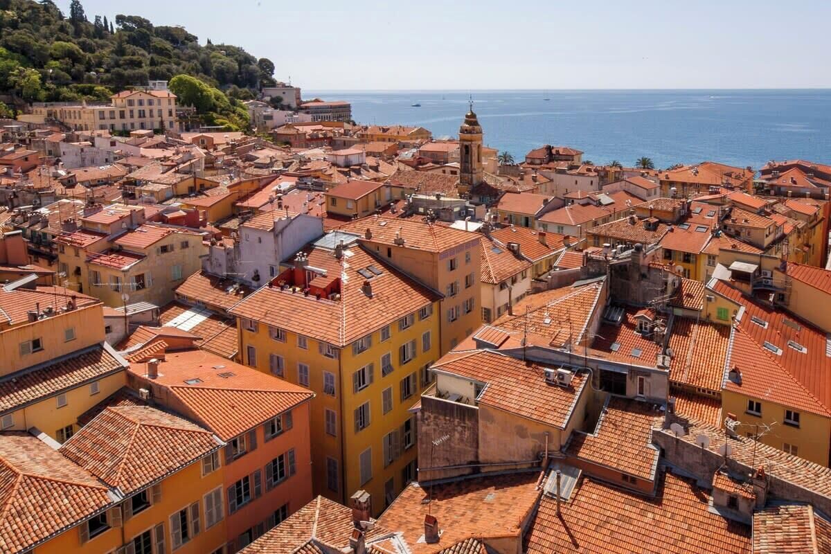 Una zona urbana densamente poblada con edificios de tejados de terracota, una imponente torre campanario y vistas al mar.