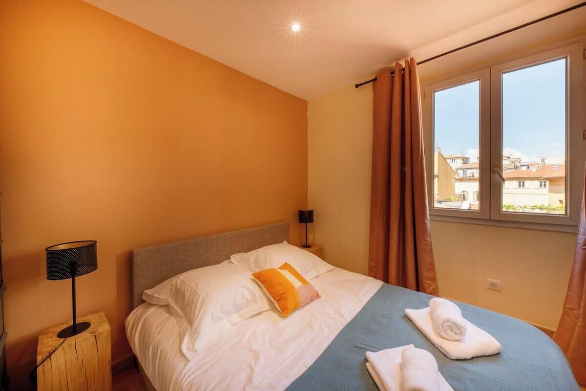 Ein Hotelzimmer mit einem Bett, einem Nachttisch mit Lampe und einem Fenster mit Vorhängen.