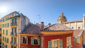 Une rue étroite bordée de bâtiments aux couleurs vives, un café avec des tables en terrasse et, au fond, une structure en forme de dôme.