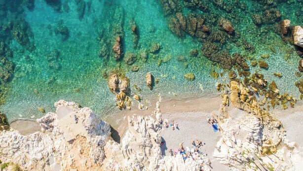 Une plage côtière avec une eau claire, des formations rocheuses et des gens qui prennent un bain de soleil.