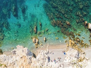 A coastal beach with clear water, rocky formations, and people sunbathing.