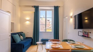 Un espace de vie compact comprenant un coin repas, un canapé, un téléviseur et une fenêtre avec des rideaux.