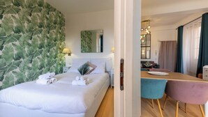 Une chambre d’hôtel comprenant un lit, un coin repas avec des chaises et une table, un miroir et un mur orné d’un motif végétal.