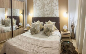 Une chambre d’hôtel avec un grand lit, deux tables de chevet avec des lampes, un miroir et un mur décoratif orné de motifs de feuilles.