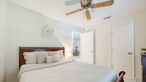 A bedroom with a wooden bed, white bedding, a ceiling fan, and a white door.